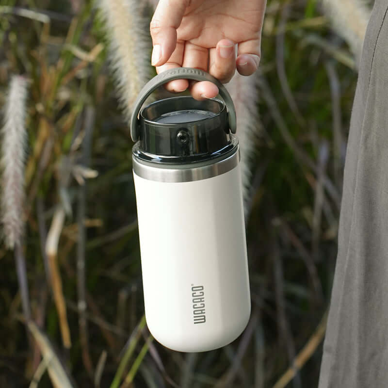 Person holding an insulated coffee cup with a push-button lid from Wacaco, showcasing the EXAFLOW design.